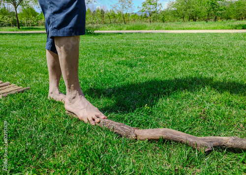 Shot with a close-up on the feet of a Caucasian man walking barefoot: he walks on a branch resting on the grass, it is a stretch of path in nature. Nice sunny day.