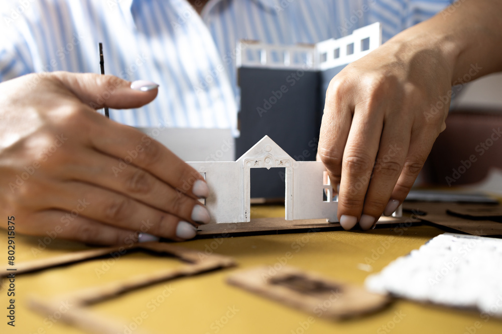 A girl assembles a model of a building from thick cardboard.