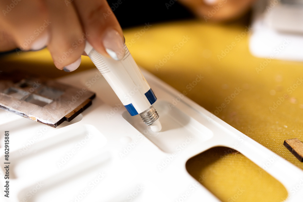 A girl squeezes acrylic paint from a tube onto an art palette. A woman is preparing to paint with white paint.