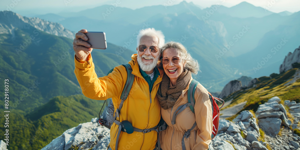 Cheerful senior hiker couple taking a selfie atop of a mountain they just hiked. Adventurous elderly man and woman with backpacks. Hiking and trekking on a nature trail.