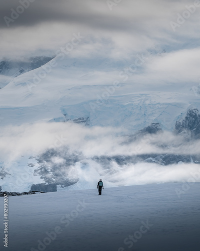 person walking on the ice of Antarctica with clouds and mountains in the back 