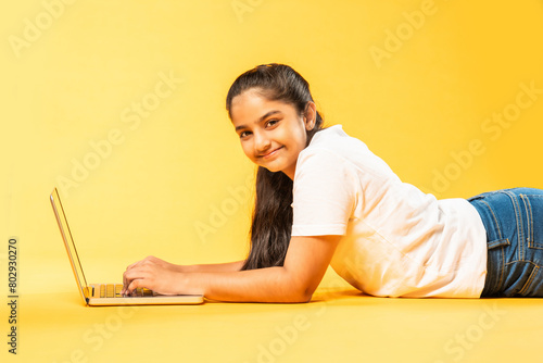 Indian asian schoolgirl using laptop on yellow background photo