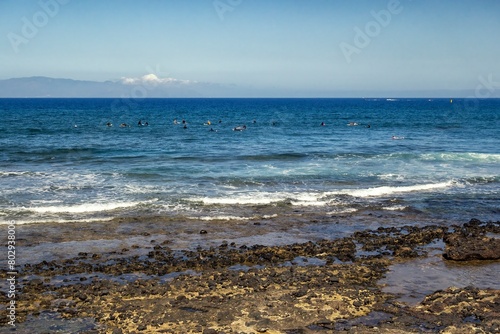 Beach on the island of Tenerife formed with volcanic rocks with the Atlantic Ocean and some surfers in the background