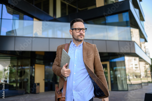 Quadro em tela Confident manager with laptop looking away and walking on street against modern