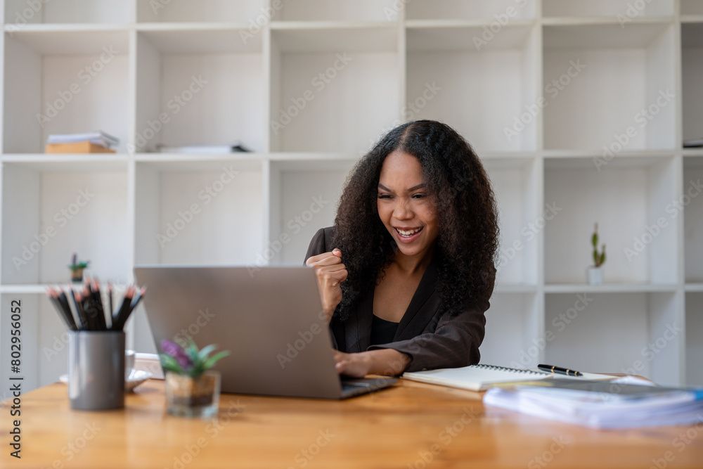 A woman is sitting at a desk with a laptop and a notebook. She is smiling and she is happy A woman is sitting at a desk with a laptop and a notebook. She is smiling and she is happy