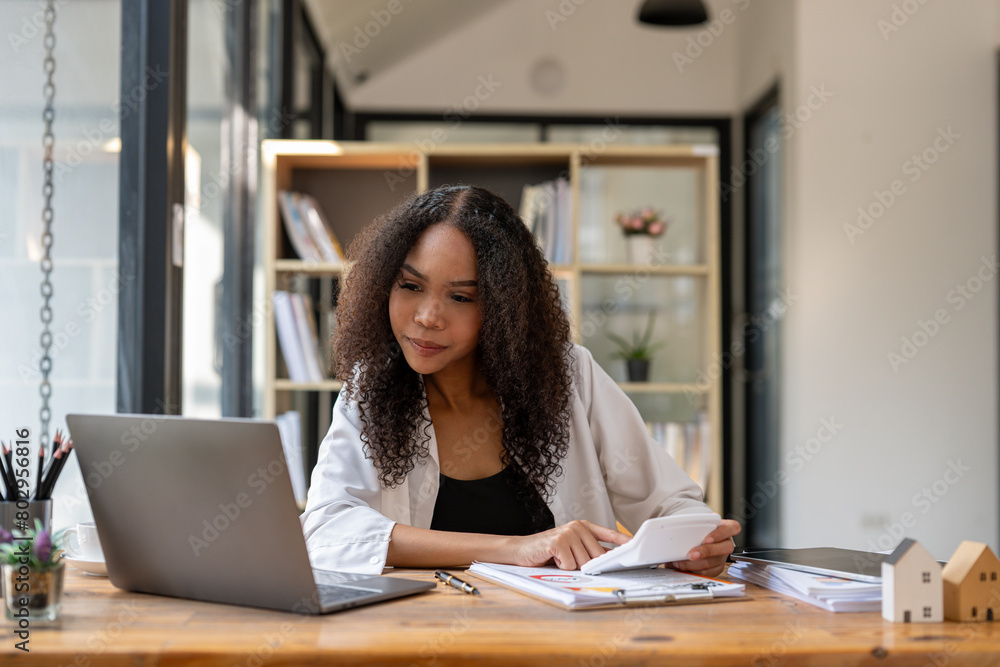 A woman is sitting at a desk with a laptop and a stack of papers. She is looking at the papers and seems to be focused on her work. Concept of productivity and concentration A woman is sitting at a desk with a laptop and a stack of papers. She is looking at the papers and seems to be focused on her work. Concept of productivity and concentration