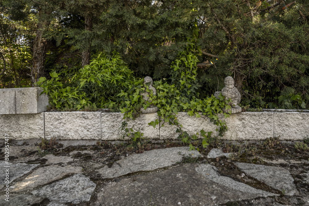 Perimeter fence of a garden with hedges and decorative stone objects and slabs of the same material on the ground Perimeter fence of a garden with hedges and decorative stone objects and slabs of the same material on the ground