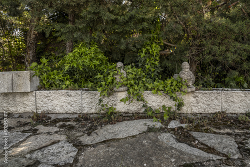 Perimeter fence of a garden with hedges and decorative stone objects and slabs of the same material on the ground