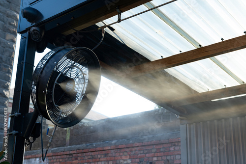 Water mister fan blows cool water into the air to cool down the area outside on a hot summer day