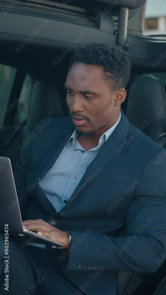 Vertical Screen: Man with laptop sitting inside charging electric car. Male entrepreneur sitting inside his red car with opened door and folding portable laptop on knees. Electric auto with charging Vertical Screen: Man with laptop sitting inside charging electric car. Male entrepreneur sitting inside his red car with opened door and folding portable laptop on knees. Electric auto with charging
