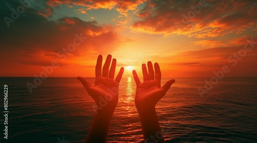 Silhouetted hands reaching towards the sunset over the ocean.