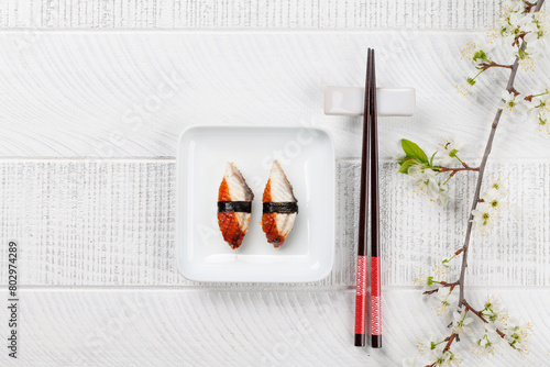 Eel sushi adorned with cherry blossom branch and chopsticks, epitomizing Japanese food culture