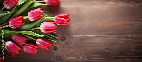 A beautifully toned photo with color tuned bouquet of fresh red tulips on a wooden table creating a border design with ample copy space image