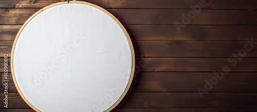 A cross stitch kit with white cotton fabric and an embroidery hoop is showcased on a wooden background offering a copy space for customization