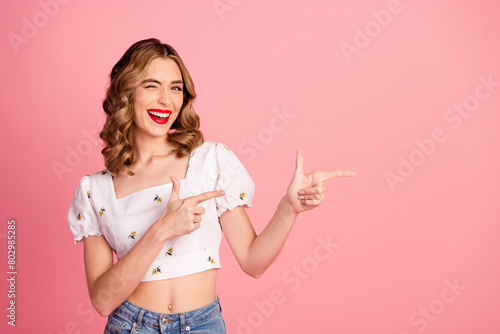 Photo portrait of pretty young girl point empty space wink flirty wear trendy white outfit hairdo isolated on pink color background