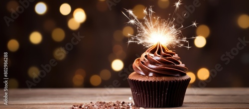 A delicious chocolate cupcake is displayed on a wooden table adorned with a sparkling sparkler creating an eye catching copy space image