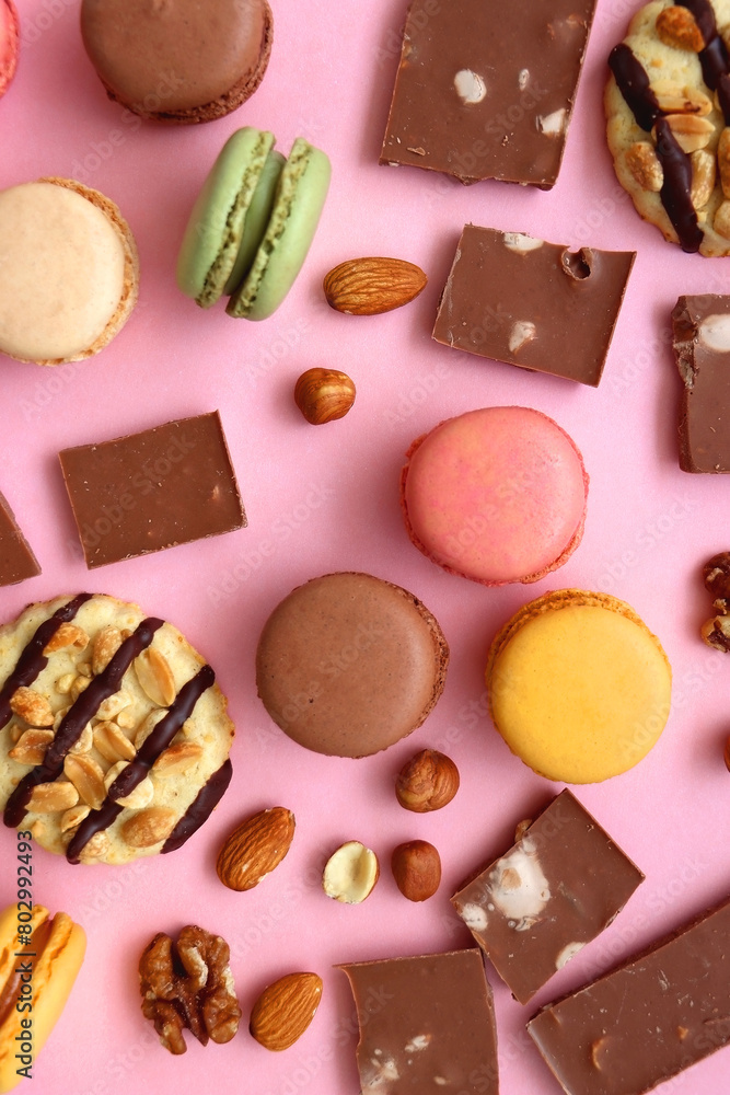 Pastel macarons, almond chocolate, peanut butter cookies and various nuts on bright pink background. Top view. Pastel macarons, almond chocolate, peanut butter cookies and various nuts on bright pink background. Top view.