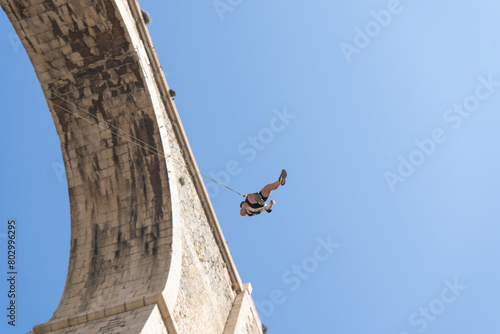 Low angle view of a person swinging after bungee jumping from a historic stone bridge. Adventure sports concept