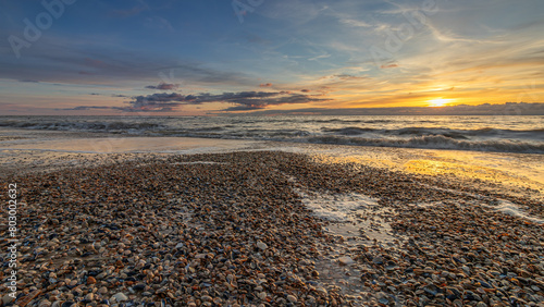 Shells on the beach of Den Helder, Netherlands, during a colorful sunset. The peak of the tide has passed, revealing the shells on the coastline. The water of the North Sea has given the shells a wash
