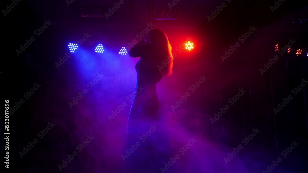 Portrait of a sexy dancer pole dance in the dark under the light of a white spotlight. Slow motion. Silhouette of a sexy girl who does a complex exercise on a pylon in the dark. Portrait of a sexy dancer pole dance in the dark under the light of a white spotlight. Slow motion. Silhouette of a sexy girl who does a complex exercise on a pylon in the dark.