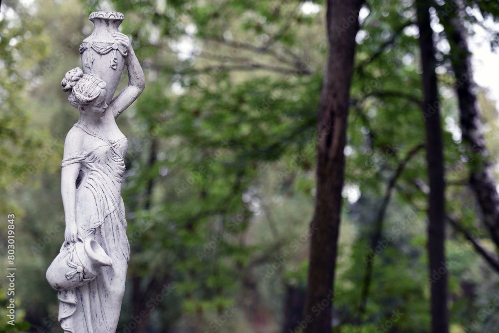 sculpture of a girl in the spring park. An old statue in a park of a semi-nude Greek or Italian Renaissance woman with a vase in a city park. in the summer garden. sculpture of a girl in the spring park. An old statue in a park of a semi-nude Greek or Italian Renaissance woman with a vase in a city park. in the summer garden.