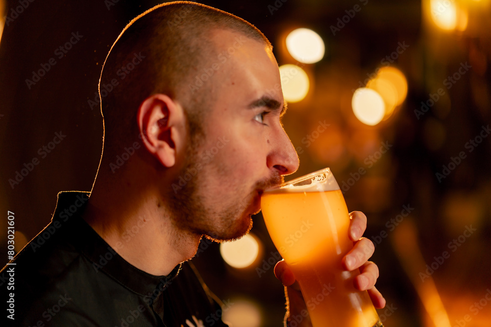 Fototapeta premium close-up on a wooden bar table guy drinks from a glass of light beer warm lighting light