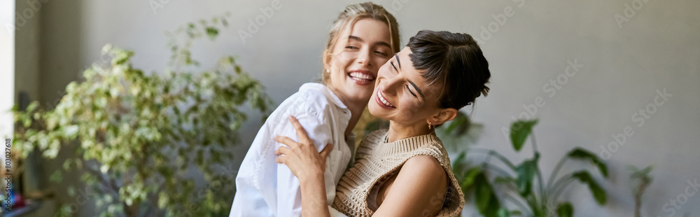 Two women, one blonde and one brunette, stand side by side in an art studio, sharing a loving moment. Two women, one blonde and one brunette, stand side by side in an art studio, sharing a loving moment.