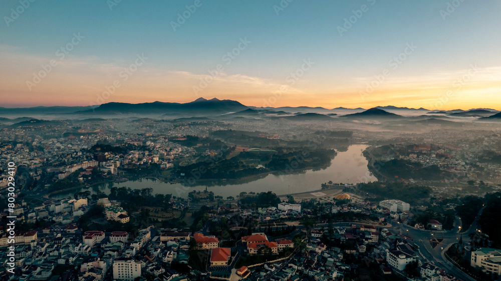 Dalat City at dawn, dusk, shrouded in mist, with diverse architecture amidst verdant greenery, nestled in rolling hills under a clear sky, exuding a serene and mystical aura