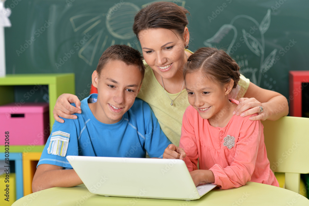 Portrait of happy mother and children sitting at table with laptop Portrait of happy mother and children sitting at table with laptop