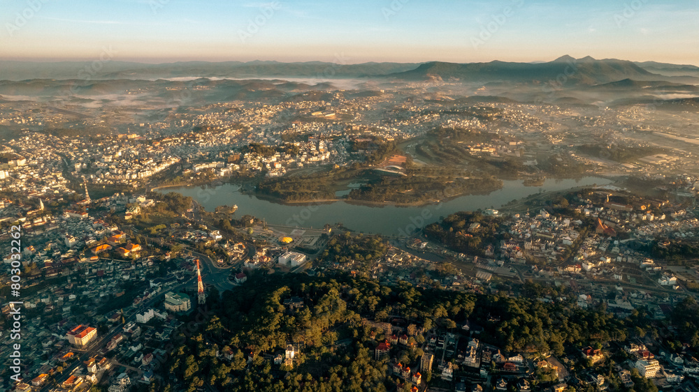 Obraz premium an aerial view of a city at sunset. The sky is ablaze with orange, pink, and purple hues, casting a warm glow on the city below. Buildings of various shapes and sizes are visible, including skyscrape