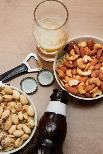 A beer glass, nuts, a bottle and a bottle cap opener on a table, close-up