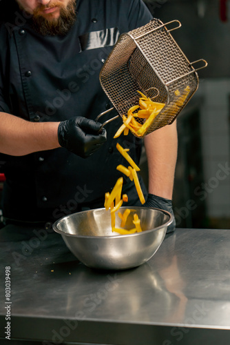 close-up in professional kitchen the chef pours French fries into an iron bowl