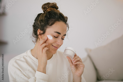 Young woman 30 years old applying face cream on her skin.