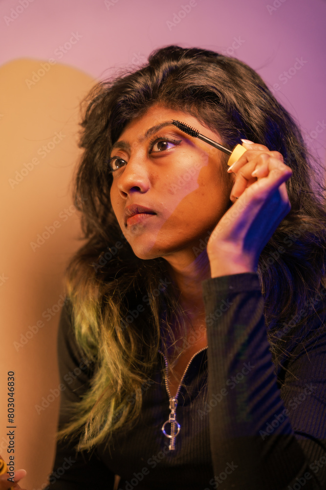 Obraz premium A woman is applying makeup, specifically mascara, to her eyes