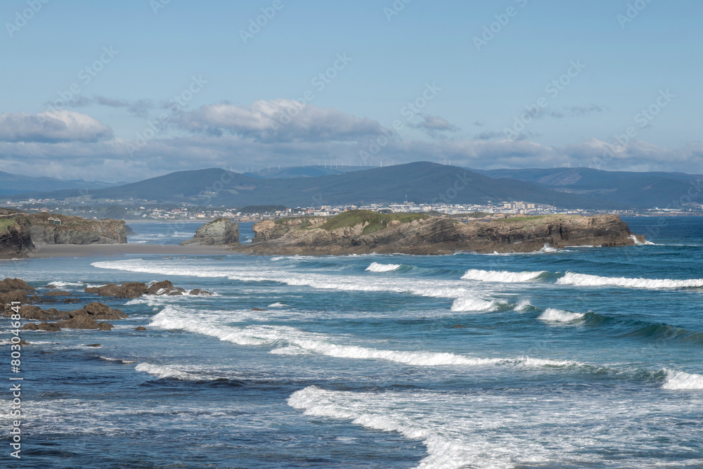 Fototapeta premium Scenic coastline, rocky shores, waves crashing, clear sky, distant mountains, peaceful exploration, untouched environment.