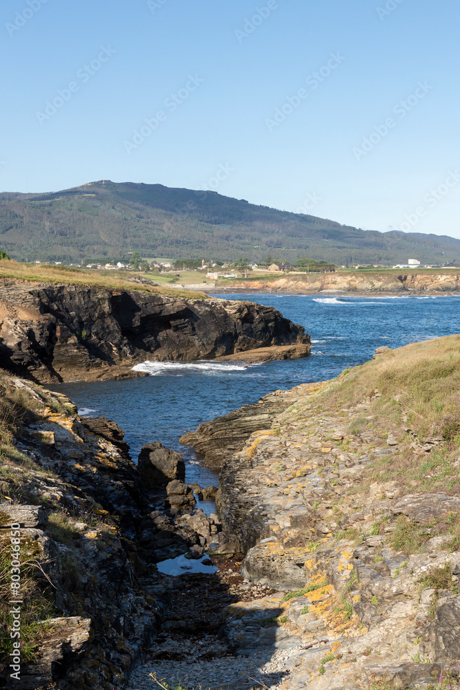 Scenic view of rocky shores, blue waters, distant mountain, clear sky, and bright day with serene natural landscape.