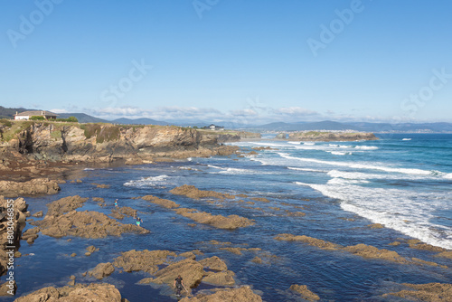 coastline, rocky shores, blue waters, waves crashing, clear sky, distant mountains, peaceful exploration, untouched environment.