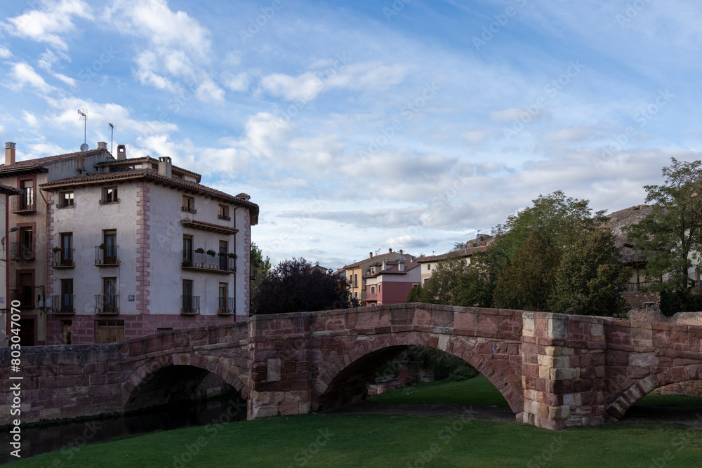 Naklejka premium a scenic view of a stone bridge, green grass, and buildings under a partly cloudy sky