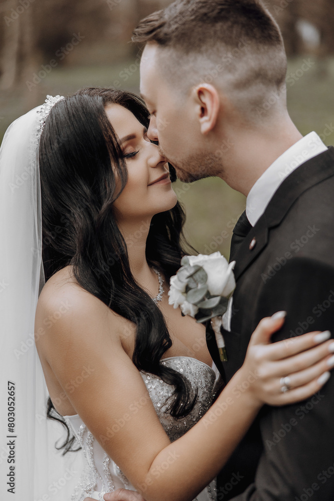 A bride and groom are kissing each other's lips. The bride is wearing a white veil and the groom is wearing a black suit A bride and groom are kissing each other's lips. The bride is wearing a white veil and the groom is wearing a black suit