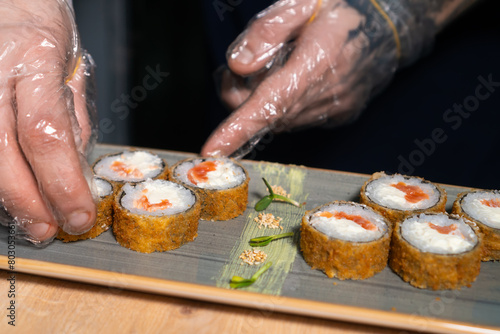 Close-up of the chef laying hot Banzai sushi with salmon, rice, cream cheese, sesame seeds, panko on a decorated plate. Concept of food