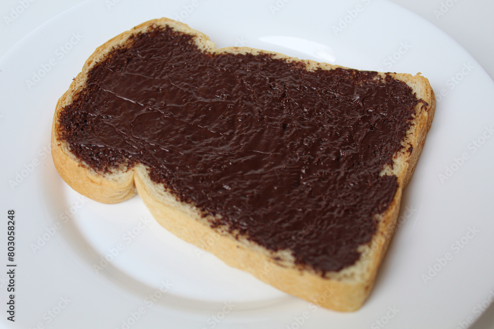 One slice of white bread, covered by chocolate spread, on white plate, isolated on white background. Prepare chocolate sandwich One slice of white bread, covered by chocolate spread, on white plate, isolated on white background. Prepare chocolate sandwich