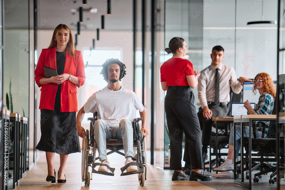 A business leader with her colleague, an African-American businessman who is a disabled person, pass by their colleagues who work in modern offices A business leader with her colleague, an African-American businessman who is a disabled person, pass by their colleagues who work in modern offices