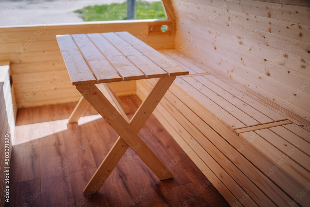 Interior shot showing a simple, natural wood table with X-shaped legs in a wooden cabin.