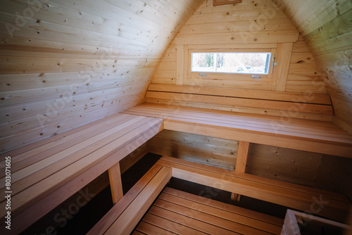 Interior view of a small cabin loft with wooden benches and a window  all surfaces covered in natural pine wood.