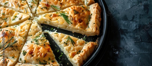 Top view of a kitchen tray filled with slices of Round Borek cheese pie baked with herbs, set against a dark background. photo