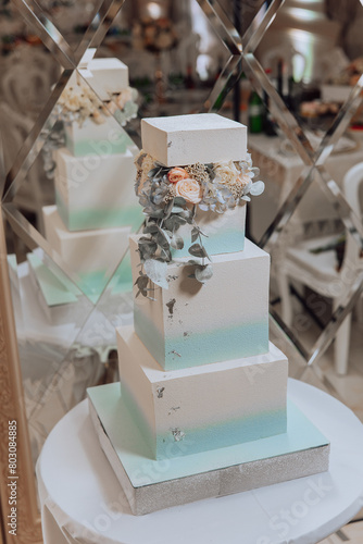 A tall white cake with blue and green stripes and flowers on top