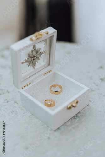 A white box with two gold rings inside. The box is decorated with a flower design