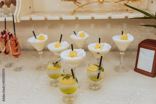 A table with a variety of drinks and desserts, including margaritas and martinis. The drinks are served in martini glasses and the desserts are in small cups