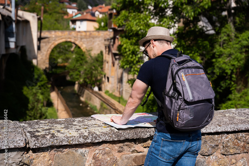 A young man explores new destinations by traveling through North Macedonia.He is standing on the bridge and looking at the map.