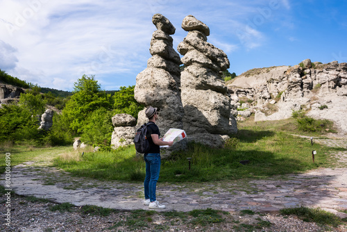 A young man explores new destinations by traveling through North Macedonia.He is standing next to stone figures and looking at a map.